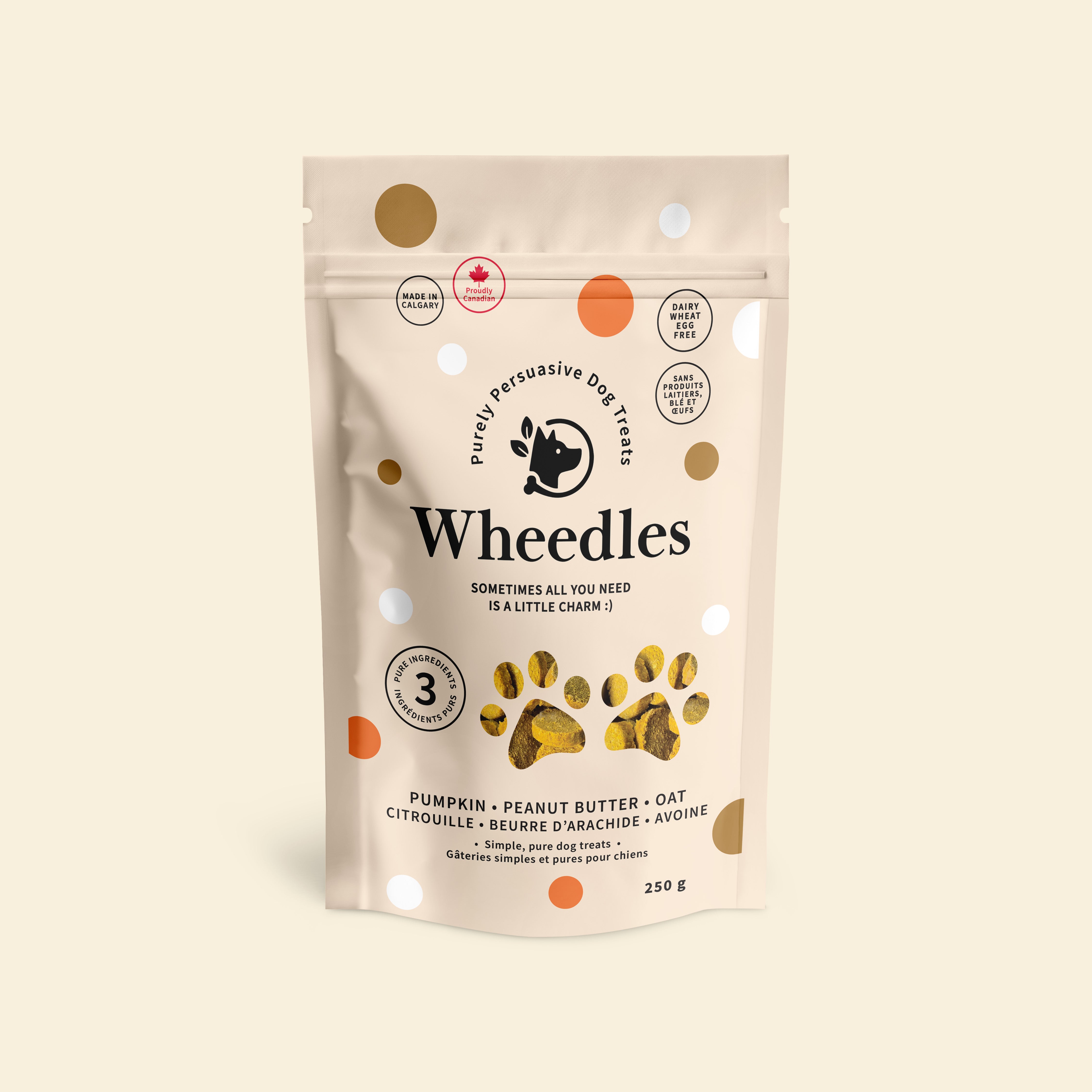 A stand-up pouch of Wheedles dog treats in peanut butter and pumpkin flavour, on a plain warm beige background. The package is off-white with scattered gold and orange dots and black text reading 'Wheedles' and 'Purely Pertussive Dog Treats.