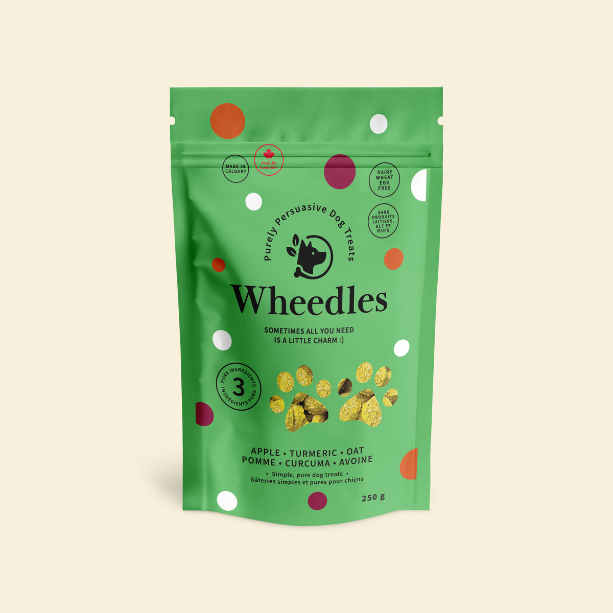 A green stand-up pouch of Wheedles dog treats in turmeric and apple flavour, on a light beige background. The packaging features white, orange, and magenta polka dots, with the brand name 'Wheedles' and product details printed on the front.
