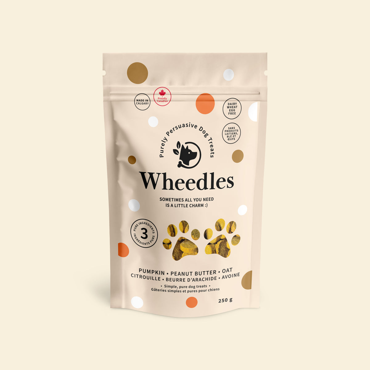 A stand-up pouch of Wheedles dog treats in peanut butter and pumpkin flavour, on a plain warm beige background. The package is off-white with scattered gold and orange dots and black text reading 'Wheedles' and 'Purely Pertussive Dog Treats.